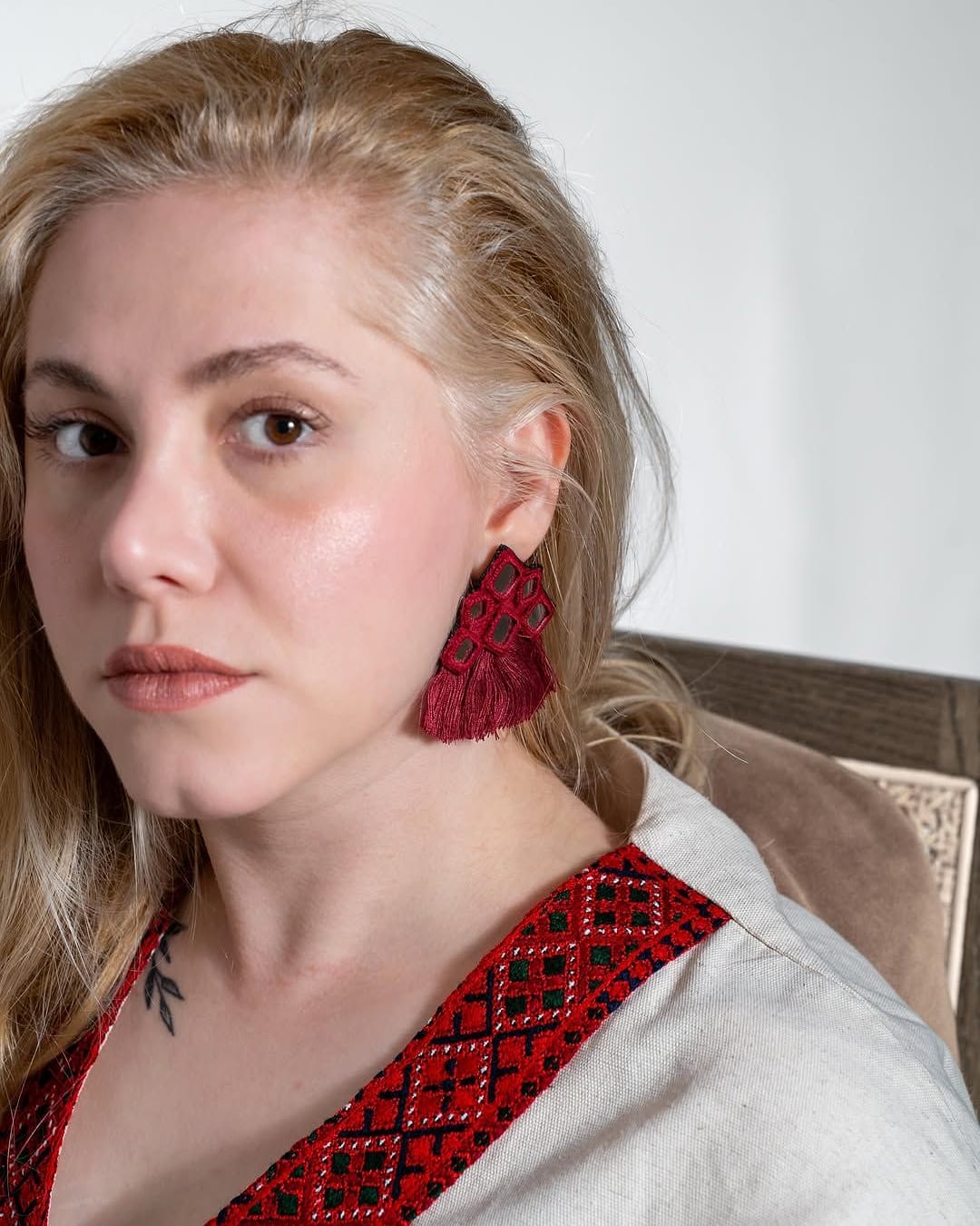 Model in a cream linen blouse with a red embroidered V neckline and red tassel earrings