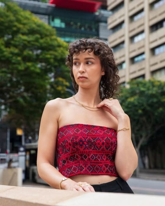 Model in a red and black embroidered strapless bandeau top, leaning on a city wall