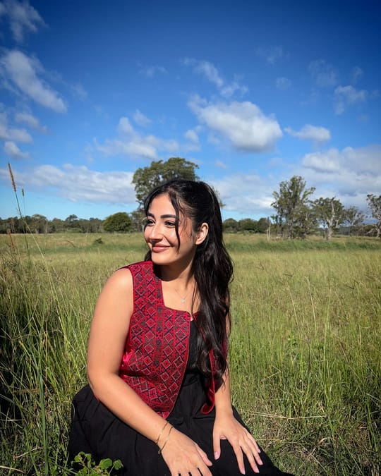 Model in a red embroidered sleeveless crop top, sitting in a grassy field