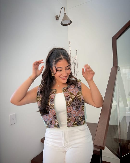 Model in a pink, brown and blue tiled embroidered vest over a white top