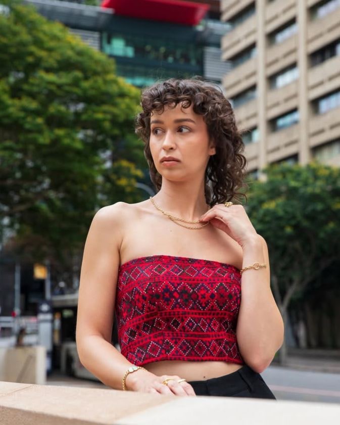 Model in a red and black embroidered strapless bandeau top, leaning on a city wall
