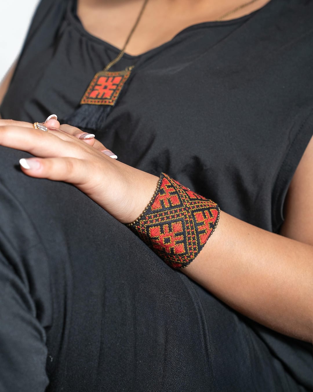 Embroidered cuff and pendant in red, orange and black worn with a black top