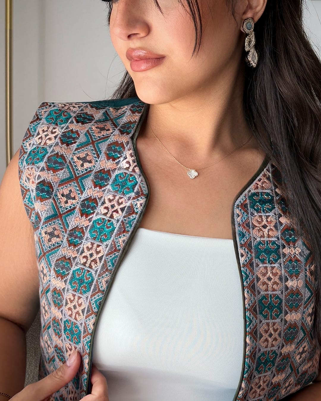 Close view of a teal, pink and cream embroidered vest over a white top