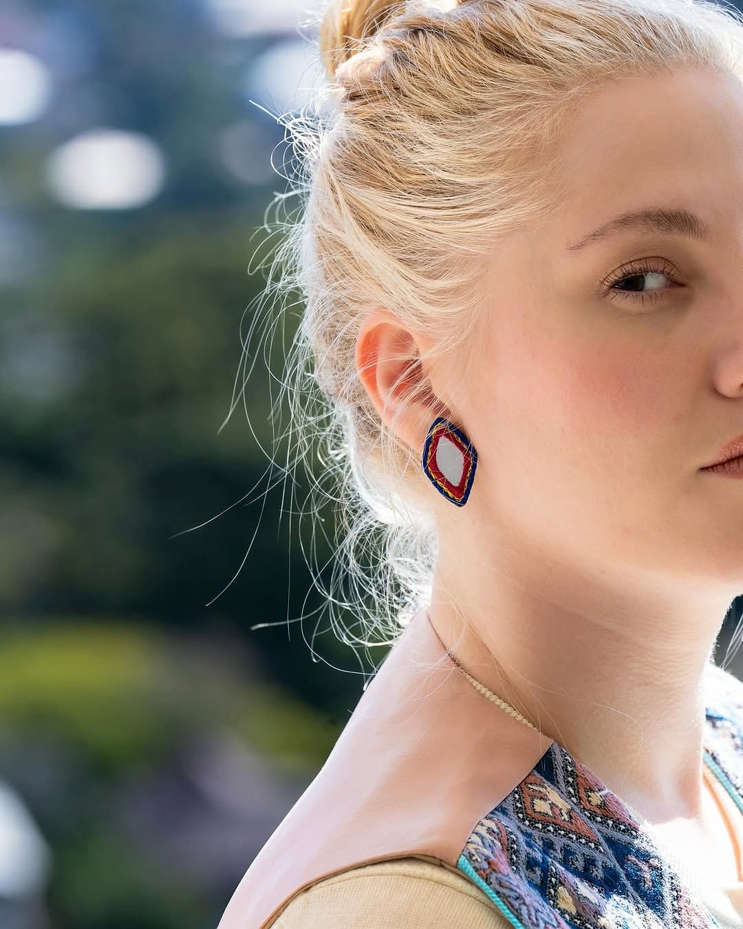 Dark red diamond shaped drop earring worn with an embroidered vest