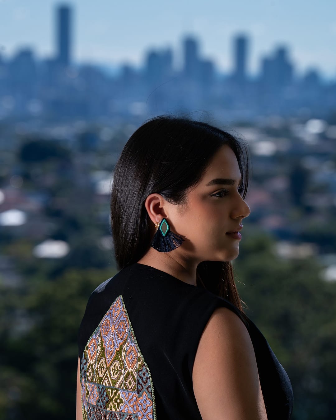 Model in profile wearing the black vest, its lilac and gold back panel showing, with a city skyline behind
