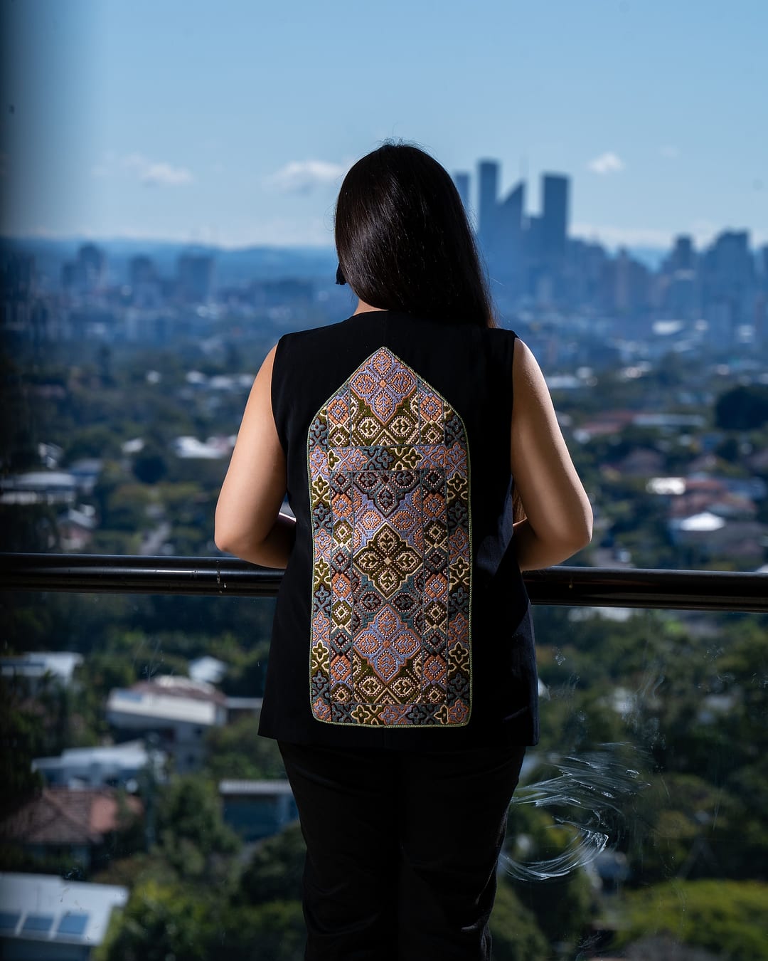Back view of a black vest with a tall lilac and gold embroidered panel