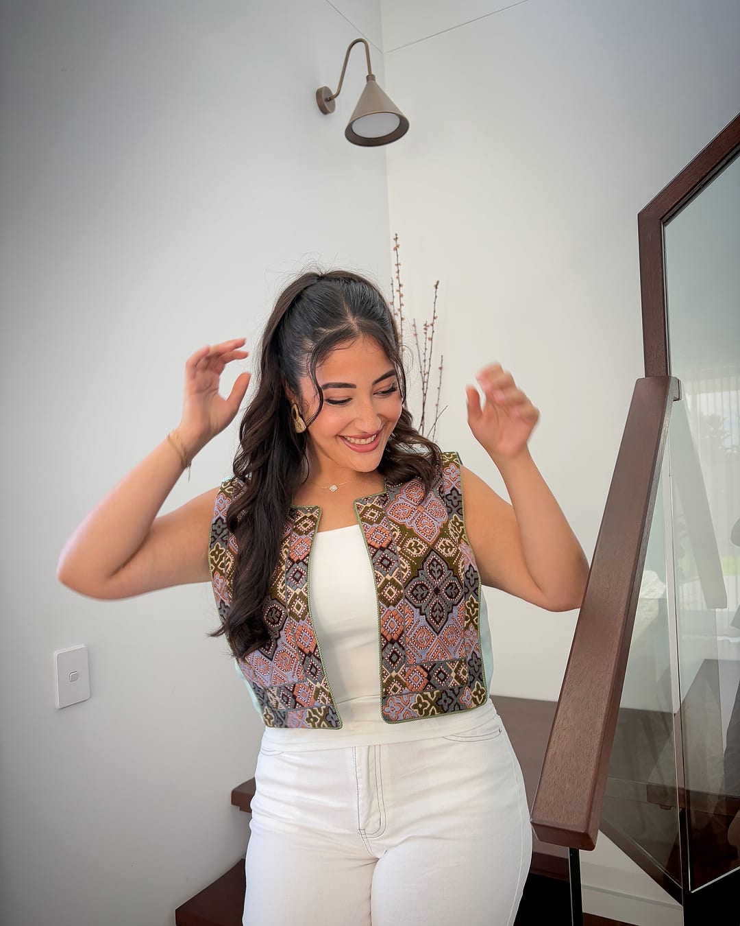 Model in a pink, brown and blue tiled embroidered vest over a white top